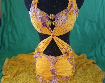 May include: A yellow dance costume with a halter top and a skirt. The top is embellished with rhinestones and flowers. The skirt is made of lace and has a ruffled hem.