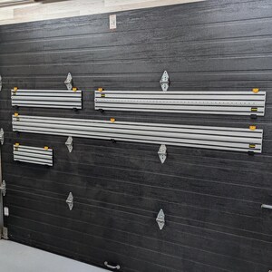 Może przedstawiać: Ciemnoszara brama garażowa z kilkoma srebrnymi i żółtymi organizerami na narzędzia zamontowanymi na niej. Organizery mają wiele szczelin i są przeznaczone do przechowywania narzędzi. Drzwi mają teksturowaną powierzchnię i srebrne zawiasy.