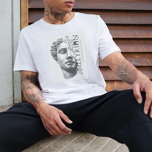 Puede incluir: Camiseta blanca con un estampado gráfico en blanco y negro de un busto de escultura con flores. El texto "ILLYRIQN" está impreso verticalmente en el lado derecho del gráfico.