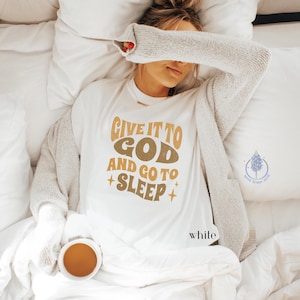 May include: White t-shirt with the text "Give it to God and go to sleep" in a retro font with gold and brown accents.