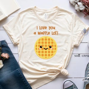 May include: A light beige t-shirt with the text "I love you a waffle lot!" and a cartoon waffle with a smiling face.