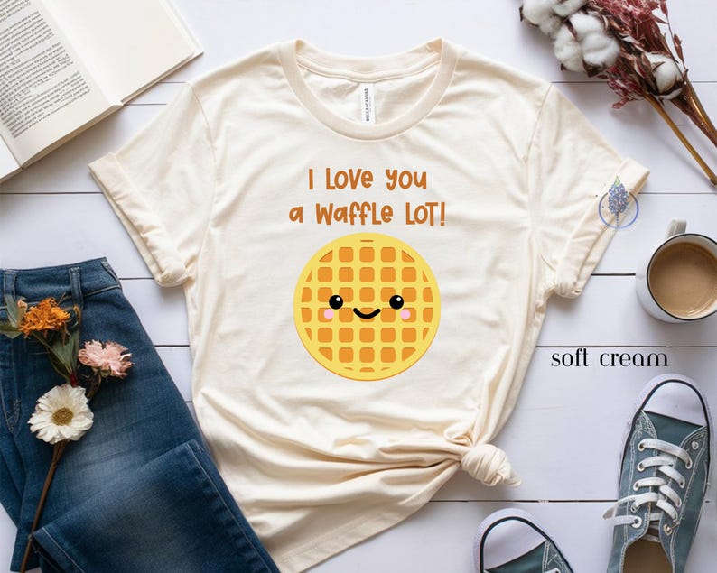 May include: A light beige t-shirt with the text "I love you a waffle lot!" and a cartoon waffle with a smiling face.