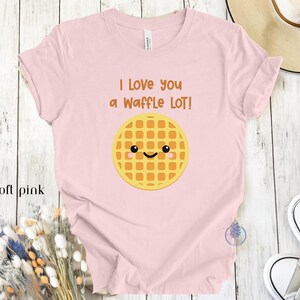 May include: A soft pink t-shirt with the text "I love you a waffle lot!" and a cartoon waffle with a smiling face.