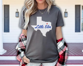Op de afbeelding: Een grijs T-shirt met een witte omtrek van de staat Texas en de tekst "Little Elm" in blauw. Een rode ster bevindt zich in het midden van de staat.