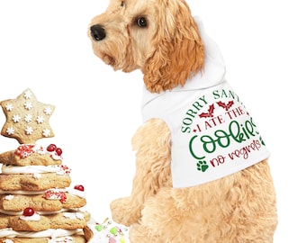 May include: A light brown dog wearing a white hooded shirt with the text "Sorry Santa I ate the cookies no regrets" in red and green. The dog is looking to the left of the image.