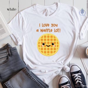 May include: White t-shirt with a cute cartoon waffle with a smiling face and the text "I love you a waffle lot!"