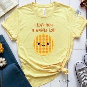 May include: Yellow t-shirt with the text "I love you a waffle lot!" and a cartoon waffle with a smiling face.