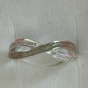 May include: A silver ring in an infinity symbol design. The ring has a band of small, clear stones on each loop. The ring is set against a white background. The ring is likely made of silver.