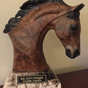 Può includere: Una scultura di testa di cavallo marrone e nero su una base di marmo bianco con una placca dorata che recita "My Art's Delight 5/22/2008 - 3/16/2018".
