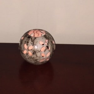 May include: A round, grey and black stone candle holder with a pink interior and cut-out designs.