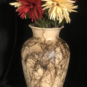 May include: A ceramic vase with a light brown background and a black crackle glaze pattern. The vase is filled with a bouquet of red, yellow, and purple flowers.