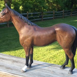 Puede incluir: Una figurita de caballo marrón con una crin y cola negras. El caballo tiene patas negras y pezuñas blancas. La figurita está de pie sobre una superficie de madera.