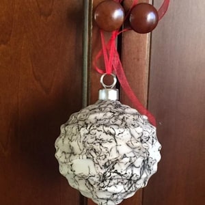May include: A white and black Christmas bauble with a textured surface. The bauble is hanging from a red ribbon.