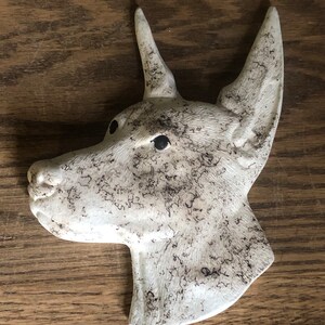 May include: White ceramic dog head sculpture with black markings. The sculpture is in profile view and has a textured surface.