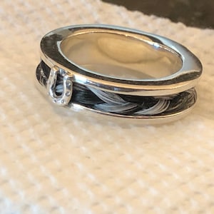 May include: A silver ring featuring a braided black and white horsehair band and a silver horseshoe charm.