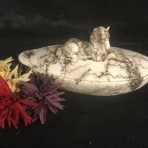 May include: White ceramic serving dish with a black and white swirl pattern. The dish has a lid with a white ceramic horse sculpture on top.