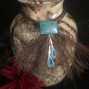 May include: A ceramic vase with a crackled glaze pattern and a turquoise stone pendant with beaded fringe hanging from the rim.