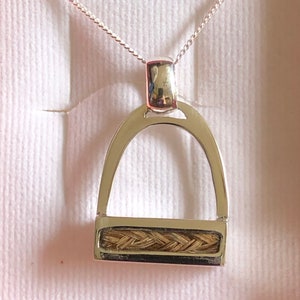 May include: A silver necklace with a silver stirrup pendant. The stirrup is filled with a braided horsehair design.