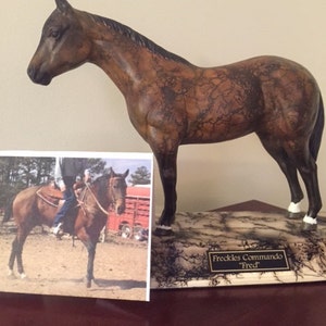 May include: A brown and black horse figurine with a black base and a plaque that reads "Freckles Commando "Fred"".