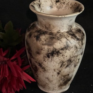 May include: A white ceramic vase with a black and white marbled design. The vase has a round body and a flared top.