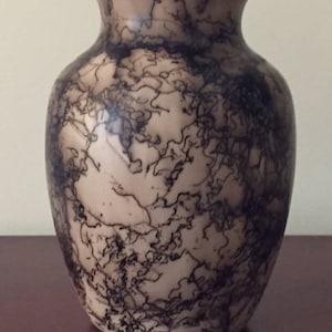 May include: A white ceramic vase with a black and brown swirling pattern. The vase has a round body and a narrow neck.