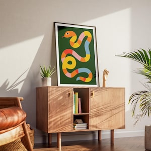May include: A framed print of a colourful abstract snake design on a dark green background. The snake is made up of geometric shapes in shades of orange, yellow, pink, blue, and red.