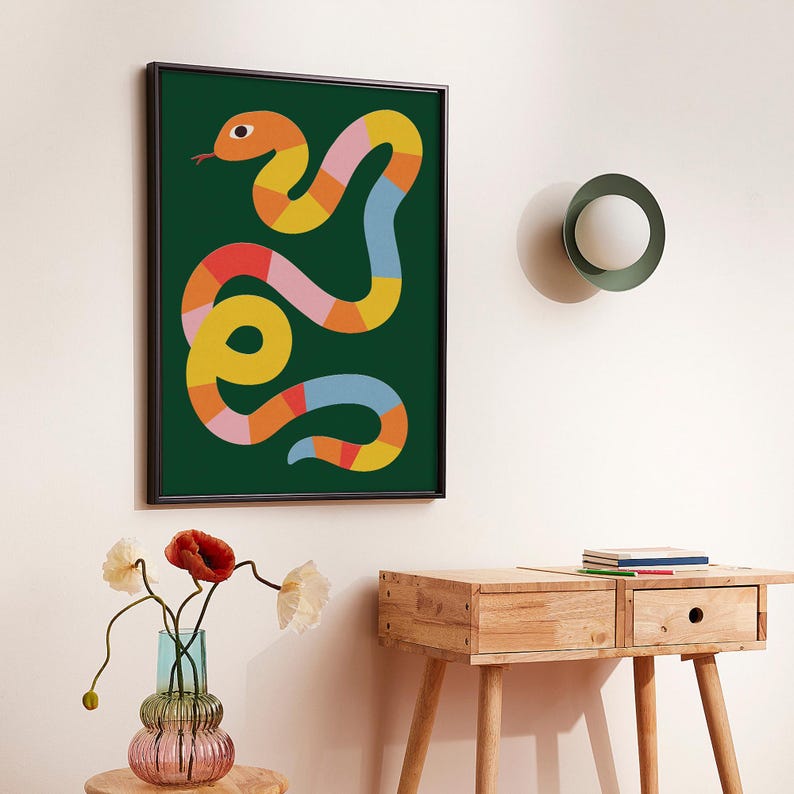 May include: A colourful abstract snake illustration in a dark green frame. The snake is made up of pink, yellow, orange, and blue segments. The frame is dark brown wood.