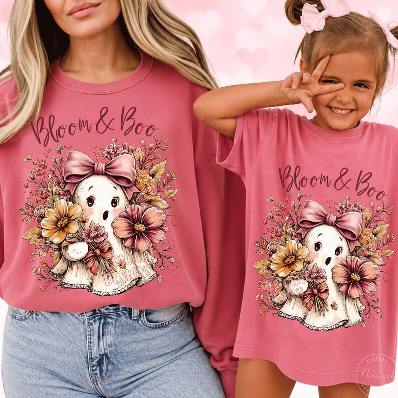 May include: A dusty rose long-sleeve sweatshirt and a matching short-sleeve t-shirt, both featuring a graphic of a white ghost wearing a pink bow, surrounded by colorful flowers and the text Bloom & Boo in a dark script font.