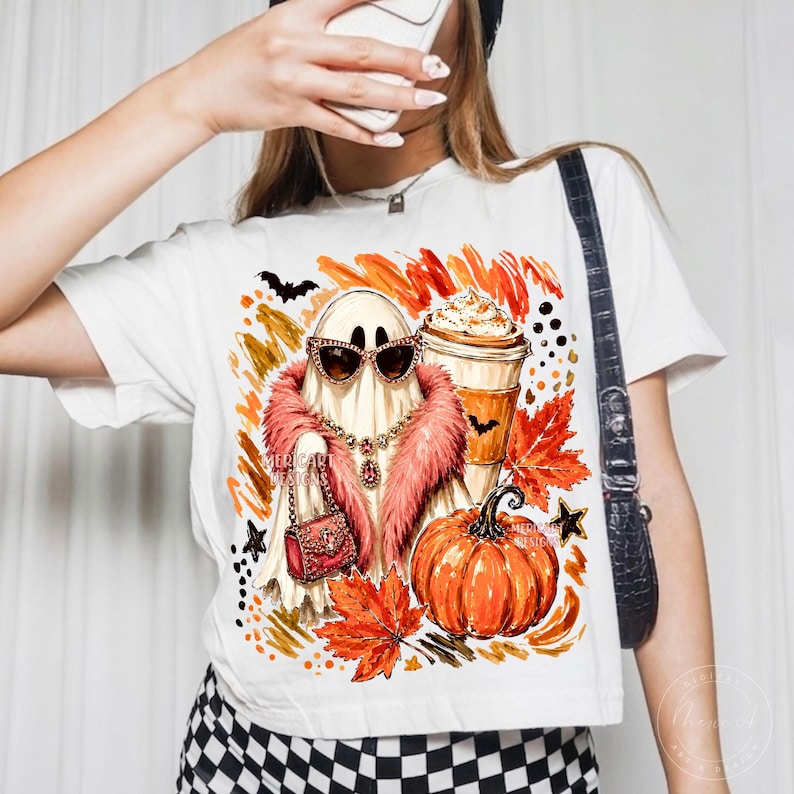 Puede incluir: Una camiseta blanca con un estampado gr&aacute;fico de un fantasma con gafas de sol, una estola de piel sint&eacute;tica rosa y un bolso. El dise&ntilde;o incluye una calabaza, una taza de caf&eacute; con nata, hojas de oto&ntilde;o y murci&eacute;lagos con el texto Mericart Designs.