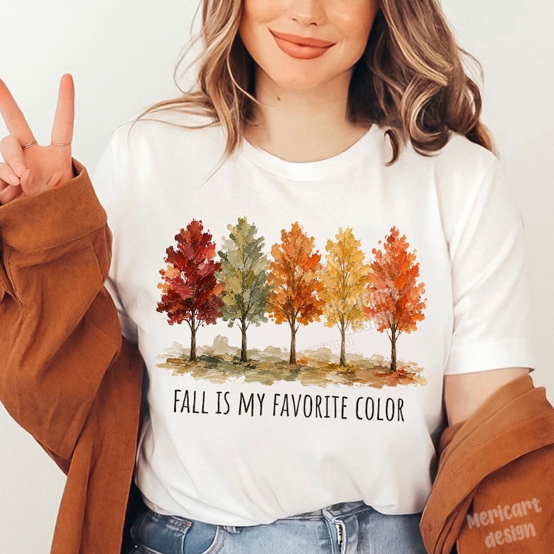 K&ouml;nnte beinhalten: Ein wei&szlig;es kurz&auml;rmeliges T-Shirt mit einer Grafik von f&uuml;nf stilisierten B&auml;umen in herbstlichen Farben wie Rot, Gr&uuml;n, Orange und Gelb. Unter den B&auml;umen steht der Text FALL IS MY FAVORITE COLOR in schwarzen Gro&szlig;buchstaben.