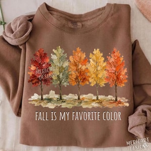 K&ouml;nnte beinhalten: Ein braunes Sweatshirt mit Rundhalsausschnitt und einer Grafik von f&uuml;nf B&auml;umen mit herbstlich gef&auml;rbten Bl&auml;ttern in Rot-, Gr&uuml;n-, Orange- und Gelbt&ouml;nen. Unter den B&auml;umen steht der Text "FALL IS MY FAVORITE COLOR" in wei&szlig;en Gro&szlig;buchstaben.