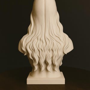 May include: A cream-colored bust sculpture depicting a person with long, flowing hair. The sculpture is set on a rectangular base and is viewed from the back. The hair cascades down the back in wavy strands.