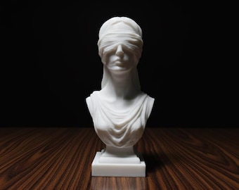 May include: A white marble bust of Lady Justice, blindfolded, with draped clothing. The sculpture is on a square base, set against a dark background and a wooden surface.