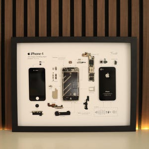 Könnte beinhalten: Gerahmter Druck eines zerlegten iPhone 4, das seine internen Komponenten zeigt. Der schwarze Rahmen umgibt einen weißen Hintergrund mit den Teilen des Telefons in einer Explosionsansicht. Das Apple-Logo ist auf der Rückseite des Telefons zu sehen.