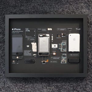 Może przedstawiać: Oprawiona czarna ekspozycja przedstawiająca iPhone'a i jego komponenty. Ekspozycja zawiera kompletnego iPhone'a, rozebrany telefon i różne części wewnętrzne. Logo Apple jest widoczne. Tekst na wyświetlaczu brzmi "iPhone Apple na nowo wynajduje telefon."