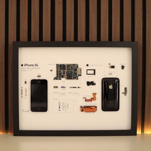 May include: Framed artwork featuring an exploded view of an iPhone 3G, showcasing its components. The black frame surrounds a white background with the phone's parts arranged. The phone's front and back are displayed, along with the internal circuit board.