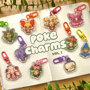 May include: A collection of ten clear acrylic charms featuring colourful cartoon character illustrations, each attached to a plastic lobster clasp in various colours including pink, orange, green, yellow, and purple. The text Poke Charms Vol. 1 is visible.