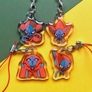 Puede incluir: Cuatro llaveros de acrílico transparente con personajes de dibujos animados en naranja, azul y blanco. Cada llavero tiene un cierre plateado y un cordón rojo. El fondo es una mezcla de amarillo y verde.