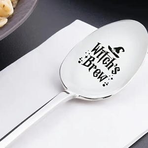 May include: A silver serving spoon with a black design that says "Witch's Brew" with a witch's hat above the text.