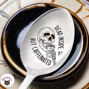 May include: White ceramic spoon with a black and white illustration of a skull drinking coffee. The text "Dead Inside But Caffeinated" is written on the spoon.