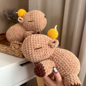 Op de afbeelding: Twee bruine gehaakte knuffels met gele gehaakte vruchten erop. De dieren liggen en hebben een zachte, pluche textuur.