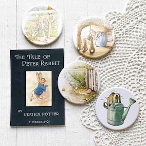 May include: A rectangular book cover titled The Tale of Peter Rabbit by Beatrix Potter and four circular pins featuring illustrations of rabbits. The pins depict a rabbit in a garden, a rabbit in a burrow, a rabbit near a gate, and a rabbit in a watering can.