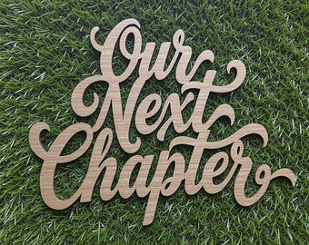 May include: A light brown wooden cutout sign featuring the words Our Next Chapter in a cursive script font. The letters are connected in a single piece with a smooth finish and visible wood grain, displaying a decorative script lettering style.