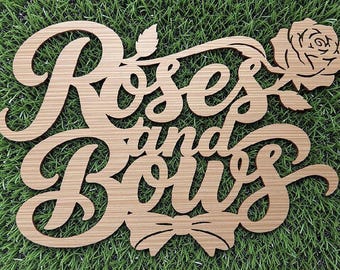 May include: A light brown laser-cut wooden sign featuring the text "Roses and Bows" in a cursive script font. The design includes a detailed rose flower at the top right corner and a small bow icon centered at the bottom of the lettering.