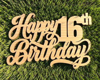 May include: A light brown wooden cake topper featuring the laser-cut text Happy 16th Birthday in a cursive script font. The sign is constructed from a single piece of wood with a visible grain pattern and smooth edges throughout the lettering.