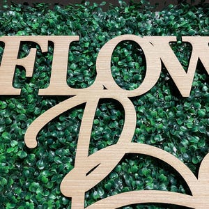 May include: Wooden sign with the words "FLOWER" and "BAR" in a cursive font. The sign is set against a backdrop of green artificial grass.