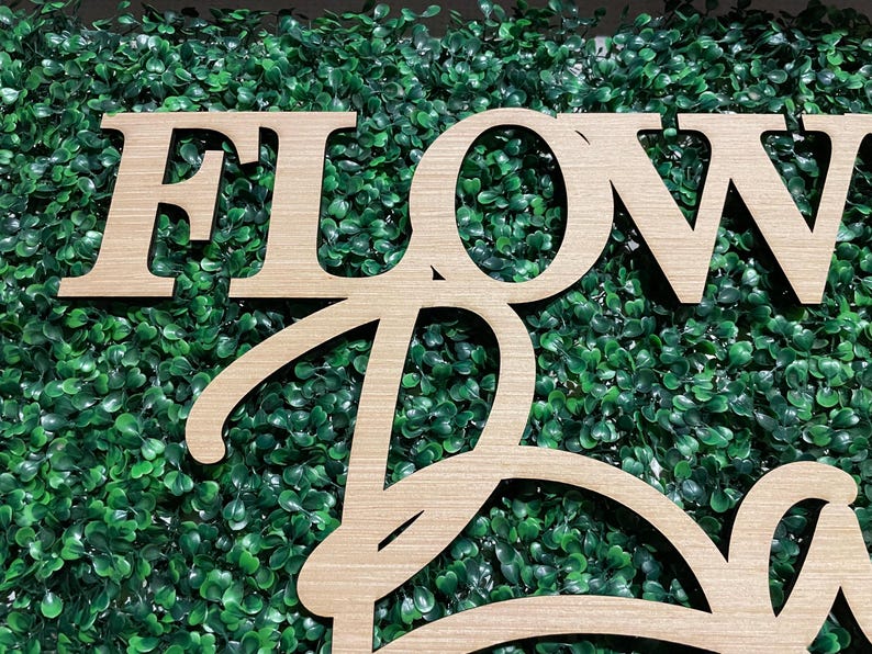 May include: Wooden sign with the words "FLOWER" and "BAR" in a cursive font. The sign is set against a backdrop of green artificial grass.