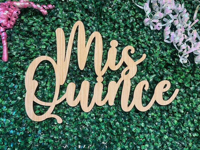 Op de afbeelding: Een lichtbruin houten uitsnede bord met de cursieve tekst Mis Quince. De letters zijn in &eacute;&eacute;n stuk verbonden met een gladde afwerking, waarbij het natuurlijke houtnerfpatroon over het gehele oppervlak van de letters zichtbaar is.