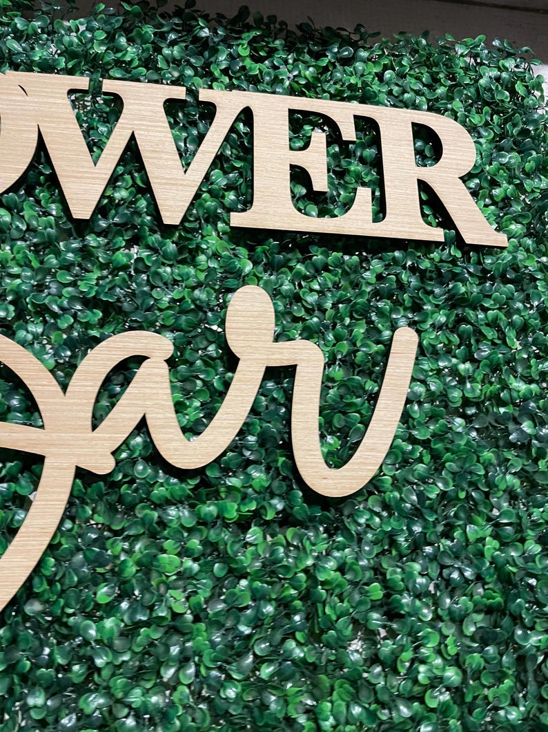 May include: Wooden sign with the words "Flower Bar" in a cursive font, set against a backdrop of green artificial foliage.
