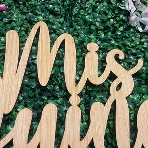 Op de afbeelding: Een lichtbruin houten uitsnede bord met de cursieve tekst Mis Quince. De letters zijn verbonden in een vloeiende schrijfstijl met een zichtbare houtnerftextuur over het gehele oppervlak, wat zorgt voor een natuurlijke en gedetailleerde uitstraling.